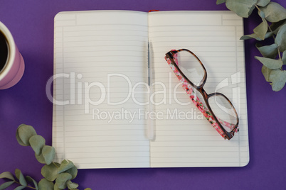 Dry leaves, black coffee, pen, spectacles and book on purple background