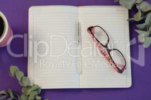 Dry leaves, black coffee, pen, spectacles and book on purple background