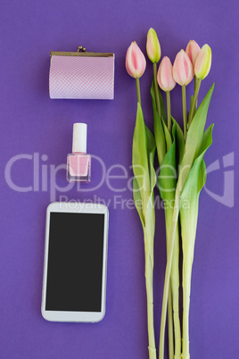 Tulips, purse, nail polish and mobile phone arranged on purple background