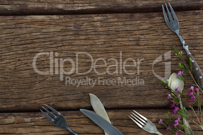 Fork, butter knife and spoon with flower on wooden table