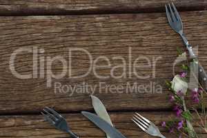 Fork, butter knife and spoon with flower on wooden table
