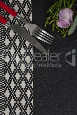 Fork and butter knife with rose flower arranged on table cloth