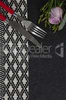 Fork and butter knife with rose flower arranged on table cloth