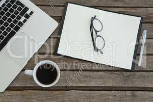 Organizer, spectacles, pen, black coffee and laptop on wooden plank