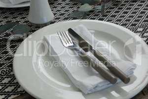 Plate with fork, butter knife and napkin on wooden table