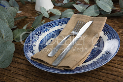 Plate with fork, butter knife and napkin on wooden table