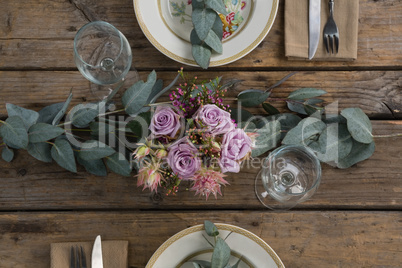Plates with napkin, fork, butter knife and flower arranged on wooden table