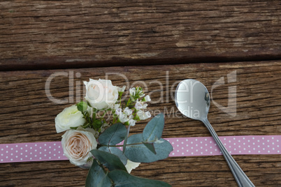 Rose flower with spoon and ribbon on wooden table