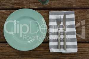 Plate with cutlery and napkin on wooden table