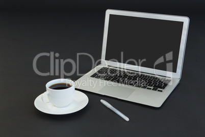 Cup of coffee, laptop and pen on black background