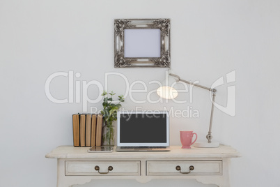 Electronic gadgets, lamp, book, mug, flora and book on table