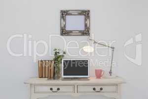 Electronic gadgets, lamp, book, mug, flora and book on table