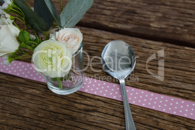 Rose flower with spoon and ribbon on wooden table