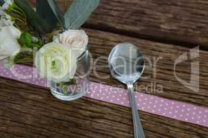 Rose flower with spoon and ribbon on wooden table