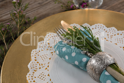 Folded napkin with cutlery and flora placed on palcemat