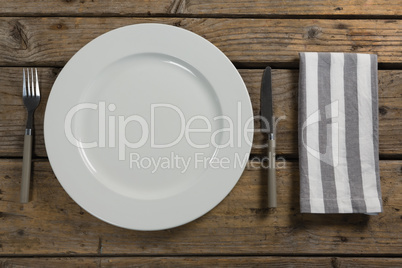 Plate with cutlery and napkin on wooden table