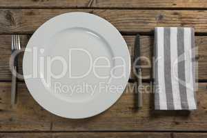 Plate with cutlery and napkin on wooden table