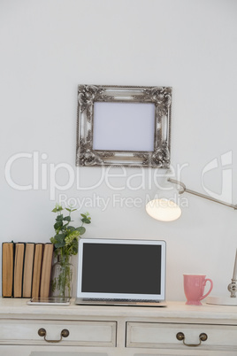 Electronic gadgets, lamp, book, mug, flora and book on table