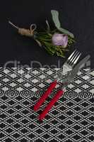Fork and butter knife with rose flower arranged on table cloth