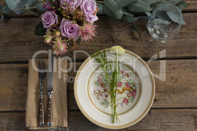 Fork and butter knife with plate and flower arranged on wooden table