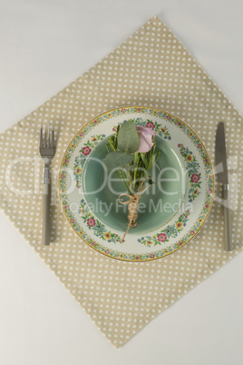 Rose flower in a bowl with cutlery on table cloth