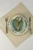 Rose flower in a bowl with cutlery on table cloth