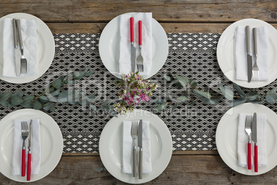 Plates with napkin, fork, butter knife and flower arranged on wooden table