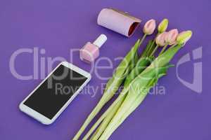 Tulips, purse, nail polish and mobile phone arranged on purple background