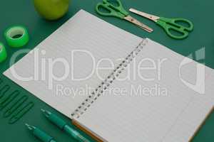 Office supplies and apple on green background