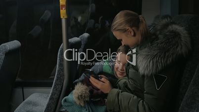 Child and mother traveling by bus and looking at photos in cellphone