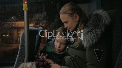 Mom and kid playing on mobile during evening bus ride