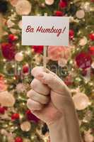 Hand Holding Ba Humbug Card In Front of Decorated Christmas Tree
