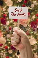 Hand Holding Deck The Halls Card In Front of Decorated Christmas