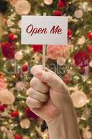 Hand Holding Open Me Card In Front of Decorated Christmas Tree.