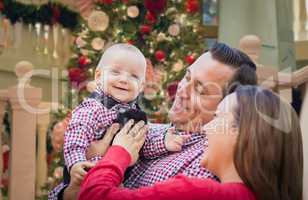Happy Young Parents with Baby In Front of Decorated Christmas Tr