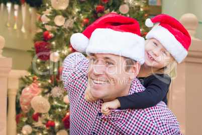 Father and Daughter Wearing Santa Hats In Front of Decorated Chr