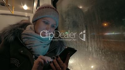 Woman using cellphone during bus ride in winter evening
