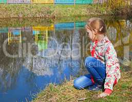 Small girl sits near the lake