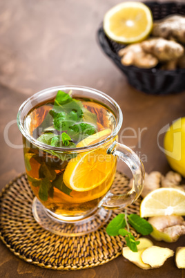 Hot herbal tea with fresh lemon, ginger and mint leaves on brown background, closeup