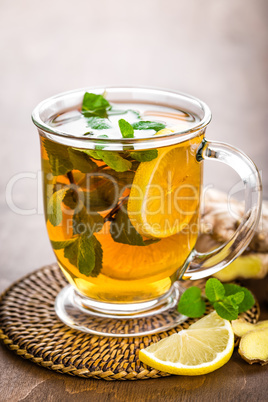 Hot herbal tea with fresh lemon, ginger and mint leaves on brown background, closeup