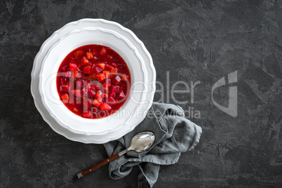 Vegetarian hot diet beetroot soup with vegetables on plate, top view, dark background