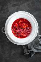 Vegetarian hot diet beetroot soup with vegetables on plate, top view, dark background