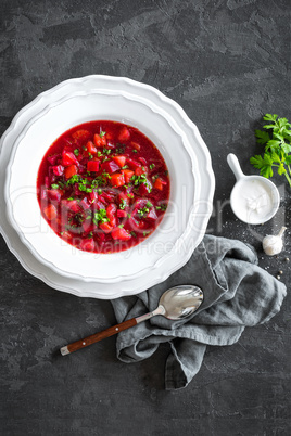 Vegetarian hot diet beetroot soup with vegetables on plate, top view, dark background