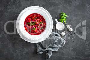 Vegetarian hot diet beetroot soup with vegetables on plate, top view, dark background