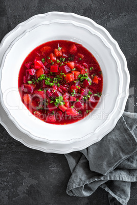 Vegetarian hot diet beetroot soup with vegetables on plate, top view, dark background