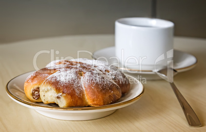 A Cup of coffee and cinnamon roll on a wooden table.