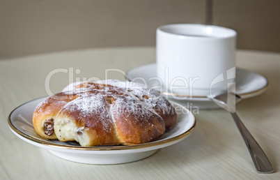 A Cup of coffee and cinnamon roll on a wooden table.