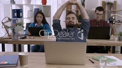 Businessman at the desk stretching arms in office