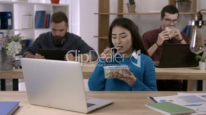 Asian businesswoman eating salad at desk in office