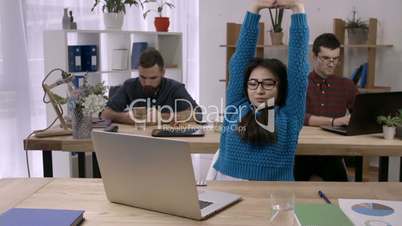 Casual businesswoman stretching at desk in office